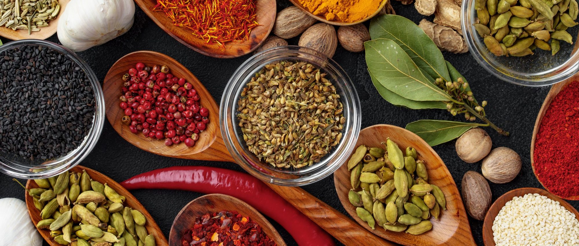 Background of variety of different vivid spices in wooden spoons, view from above